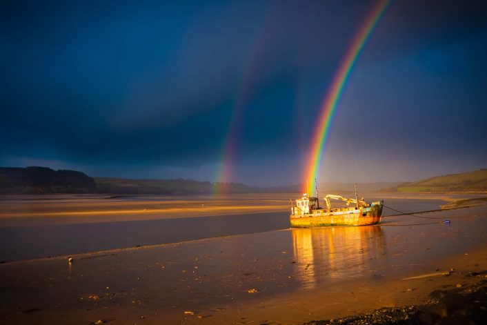 A rainbow falls over a fishing boat on the shores of the Towy estuary at Ferryside.